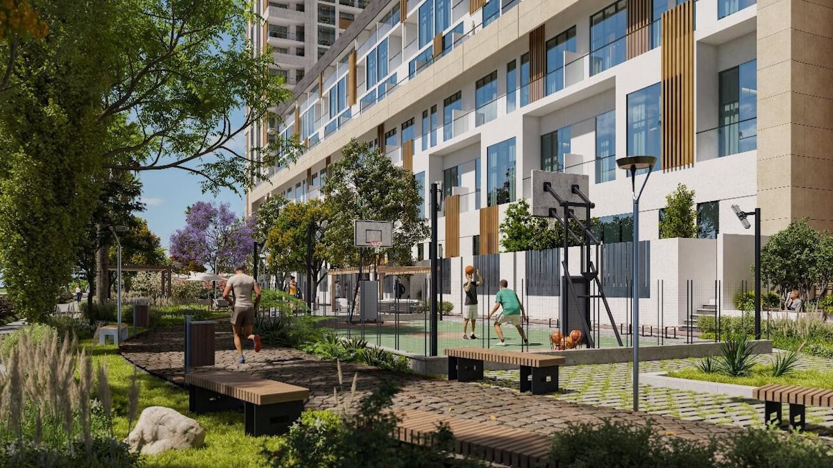 The District by Reportage features a vibrant outdoor community space with a modern apartment building in the background. The area includes a basketball court, lush greenery, benches, and people enjoying activities like jogging and playing with a dog, showcasing a luxurious and active lifestyle.